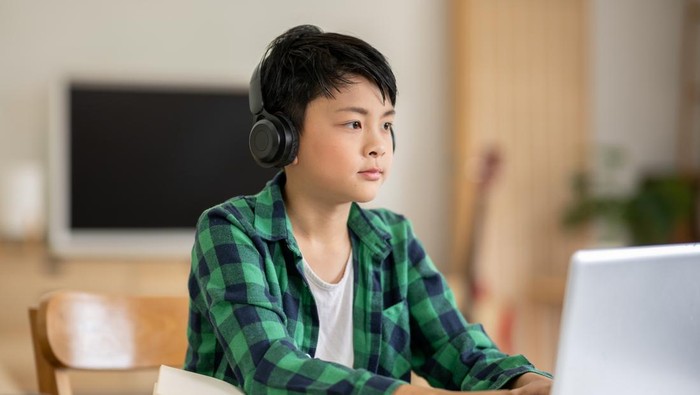 A boy is studying online intently on his laptop at home.