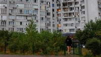 Warga lainnya hanya bisa berjalan pelan di depan gedung apartemen yang telah rusak berat, menyaksikan sisa kehancuran. REUTERS/Valentyn Ogirenko