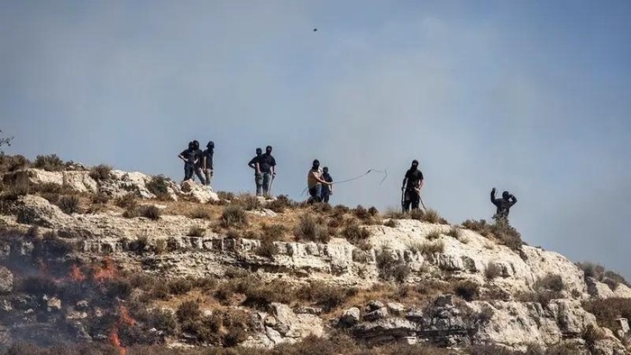 Masked Israeli settlers hurl rocks at Palestinians from hilltop in the village of Sinjil, in the occupied West Bank on July 4, 2025. (File photo: AFP)