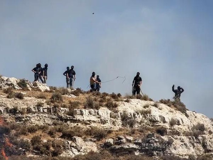 Masked Israeli settlers hurl rocks at Palestinians from hilltop in the village of Sinjil, in the occupied West Bank on July 4, 2025. (File photo: AFP)