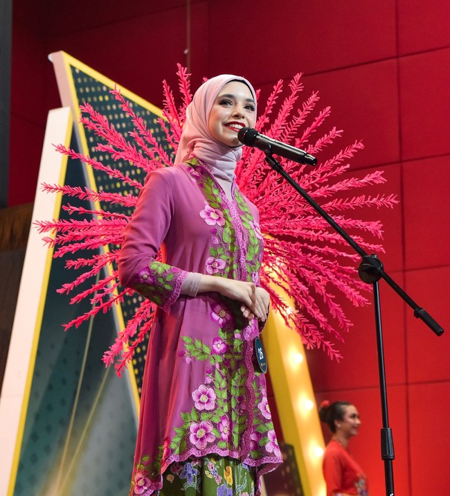 Dalam salah satu foto terlihat Isabel mengenakan kebaya ungu dengan bordir bunga-bunga cerah. Ornamen merah mencolok di latar belakang menambah kesan megah penampilannya. Ia tampak tenang dan anggun menjawab pertanyaan dewan juri. Foto: Instagram/@isabel.azhari