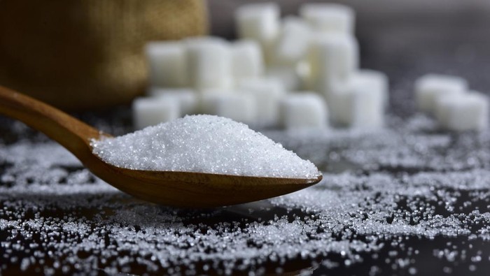 Closeup sugar piling up the shape of the hill from wooden spoons and sugar cubes on a black background. selective focus.