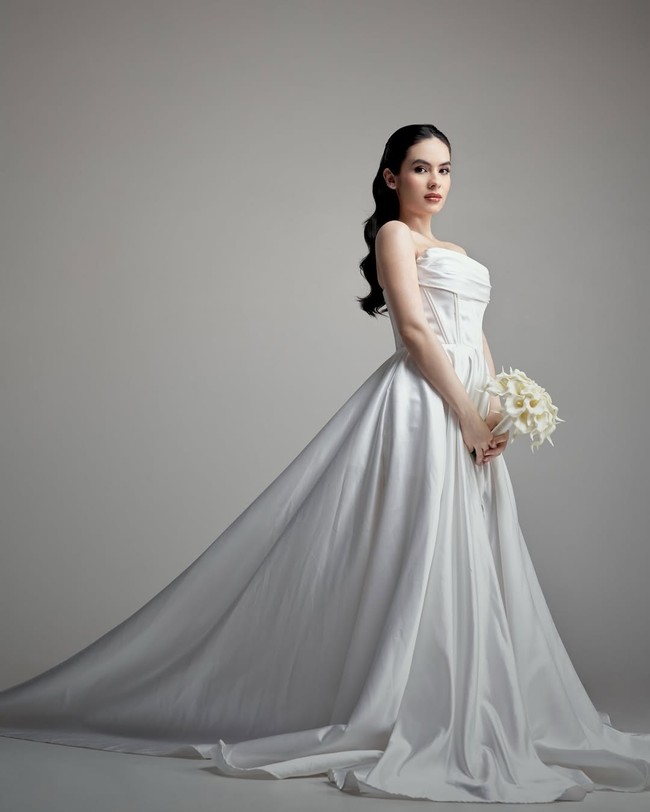 Steffi Zamora tampil anggun dalam balutan gaun pengantin putih satin yang memadukan gaya klasik dan modern minimalis. Gaun strapless dengan detail drapery di bagian dada dan potongan korset memberikan siluet feminin sekaligus tegas. Foto: Instagram/@steffizamoraaa