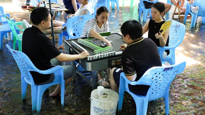 Bermain Mahjong di Sungai, Cara Unik Warga Chongqing Hadapi Gelombang Panas People play Mahjong on a shallow river amid a red alert for heat at Pianyan ancient town in Chongqing, China August 1, 2025. REUTERS/Go Nakamura