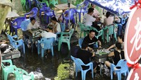 Warga mengocok keping mahjong dengan kaki terendam air sungai yang sejuk. Di tengah suhu ekstrem, permainan ini jadi pelarian dari teriknya matahari. Foto: REUTERS/Go Nakamura