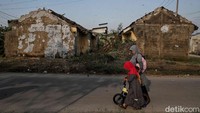 Warga melintas diantara rumah perumahan subsidi Villa Kencana Cikarang yang atap dan dindingnya rusak.