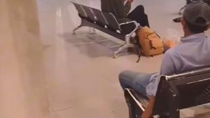 Tangkapan layar seorang pria bertopi merokok di area dilarang di pintu kedatangan Bandara Sultan Hasanuddin Makassar.