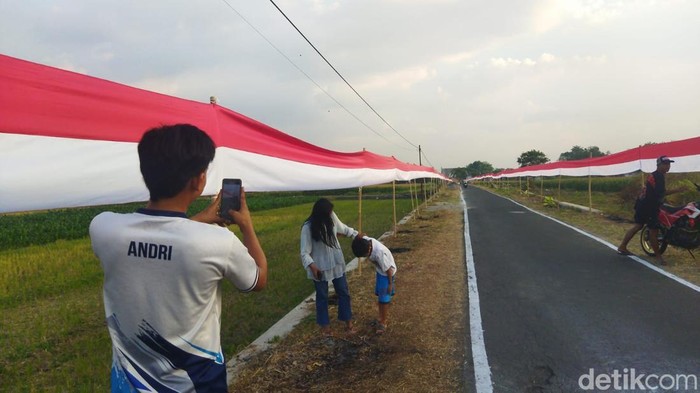 Warga saat berfoto di samping bendera Merah Putih sepanjang 800 meter yang terpasang di Desa Tarubasan, Kecamatan Karanganom, Klaten, Sabtu (2/8/2025).