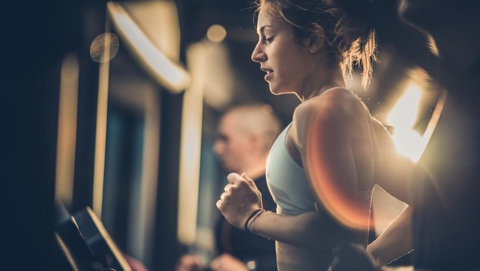 Determined female athlete jogging on treadmill in a gym while other people are beside her.