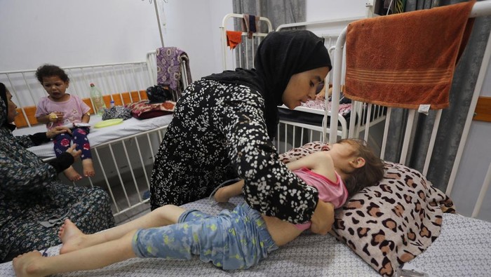 A Palestinian girl Jana Ayad, who is malnourished, according to medics, lies on a bed as her mother, Nasma Ayad, sits beside her, holding her hand, as she receives treatment at a hospital in Gaza City, amid a worsening hunger crisis, July 29, 2025. REUTERS/Mahmoud Issa