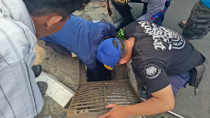 Petugas Damkar Kuningan melakukan evakuasi ponsel pedagang yang jatuh ke selokan.