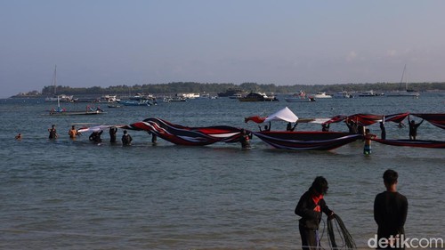 Turas dan belasan rekannya harus menarik tali dan mendaratkan layangan di laut agar tidak jatuh menukik, Minggu (3/8/2025). (Aryo Mahendro/detikBali).