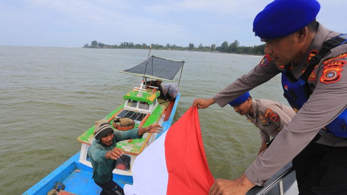 Kasat Polairud Polres Aceh Barat Iptu Karianta (kanan) membagikan bendera merah putih kepada nelayan saat patroli di Perairan Laut Meulaboh, Aceh Barat, Aceh, Senin (4/8/2025). Pembagian 80 lembar Bendera Merah Putih kepada para nelayan tersebut dalam rangka untuk menyemarakkan HUT ke-80 RI sekaligus untuk menanamkan nilai-nilai kebangsaan serta menumbuhkan semangat nasionalisme dan cinta tanah air. ANTARA FOTO/Syifa Yulinnas