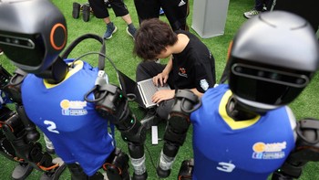 Tim mahasiswa menyesuaikan sistem navigasi robot humanoid mereka sebelum laga simulasi dimulai. Foto: REUTERS/Florence Lo