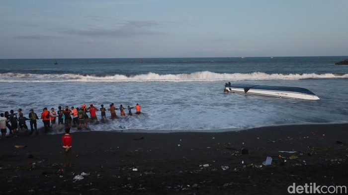 Petugas SAR Denpasar, polisi, dan warga berjibaku membalikkan badan kapal cepat yang masih terbalik di bibir Pantai Matahari Terbit, Selasa (5/8/2025). (Aryo Mahendro)