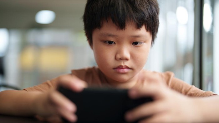 A close-up of an Asian boy sitting at a table using a smartphone