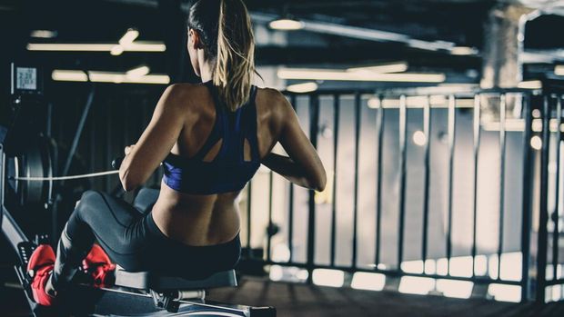 Copy space shot of an attractive young woman exercising on rowing machine in the gym. She is keeping her performance on rowing machine display.