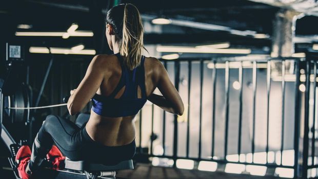 Copy space shot of an attractive young woman exercising on rowing machine in the gym. She is keeping her performance on rowing machine display.