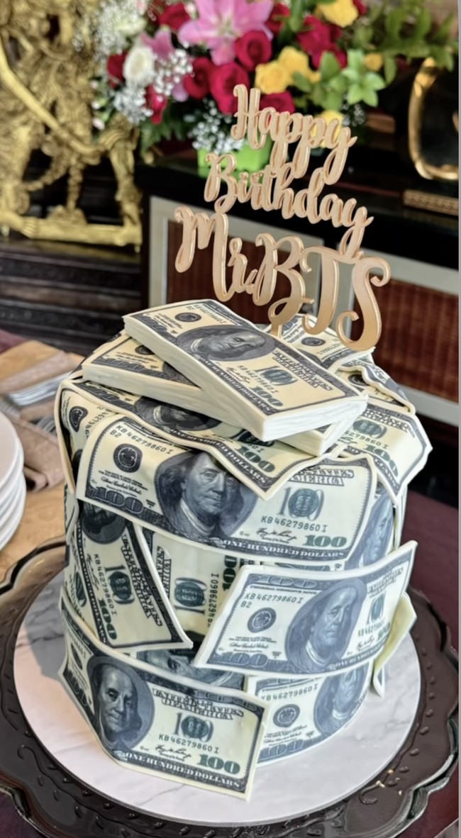 Kue ulang tahun Bambang terlihat unik dan mewah dengan dekorasi berbentuk lembaran-lembaran dollar AS. Pada bagian atasnya terdapat tulisan ‘Happy Birthday Mr. BTS’. Foto: Instagram/@mayangsari_official