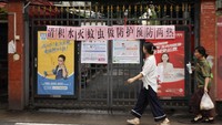 Warga melintas di depan gerbang masuk permukiman yang memajang slogan ajakan pemberantasan nyamuk di Guangzhou, Provinsi Guangdong, China, Rabu (6/8/2025). Slogan tersebut berbunyi “Mari bersama membersihkan genangan air dan memberantas sarang nyamuk”. (Feature China/Future Publishing via Getty Images)