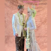 Busana Melly dan Anto diketahui berasal dari Adi Rustana Wedding Gallery. Antoo mengenakan beskap warna putih dengan hiasan bordir halus dan kancing berkilau. Bagian bawahnya memakai kain batik motif tradisional berwarna cokelat gelap dengan pola klasik. Sebagai aksesori, ia mengenakan blangkon di kepala, kalung melati panjang yang menjuntai di depan, serta keris yang terselip di pinggang. Sementara Melly tampil anggun dengan kebaya panjang warna putih perak yang dihiasi payet dan bordir mewah. Kerudungnya dilapisi mahkota siger khas Sunda yang dipadukan dengan ronce melati panjang menjuntai di kedua sisi. Bagian belakang kebaya memiliki ekor kain transparan berpayet yang menambah kesan megah. Foto: Instagram/@melly_goeslaw