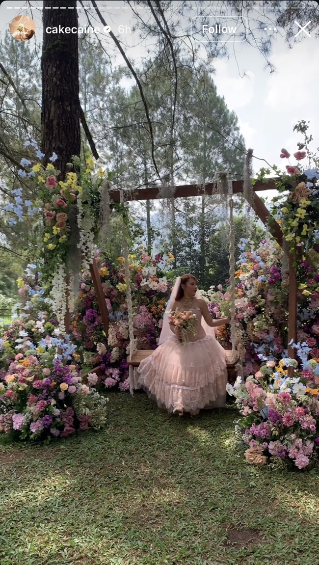 Rambutnya diikat rapi dengan sentuhan warna kemerahan yang serasi dengan tema pernikahannya. Nadin juga membawa bouquet bunga warna pastel seperti pink, peach, dan putih, berpadu dengan sedikit dedaunan segar. Foto: Instagram/@cakecaine