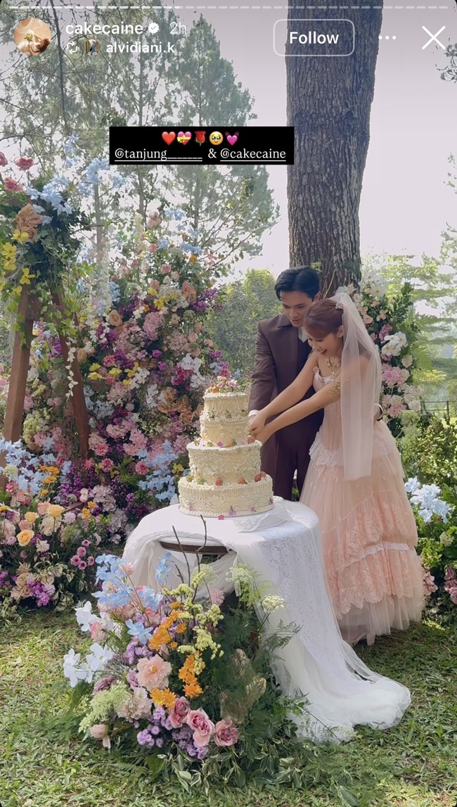 Senada dengan tema yang dipilih, kue pernikahan Nadin dan Faishal juga terlihat cantik nan elegam dengan warna putih gading berhiaskan bunga-bunga kecil warna-warni. Foto: Instagram/@cakecaine