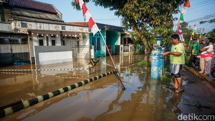 Warga beraktivitas di Perumahan Griya Satria Jingga, Bojong Gede, Kabupaten Bogor, Minggu (10/8/2025). Hujan deras sejak Sabtu (9/8) sore hingga malam membuat aliran kali di samping perumahan meluap.