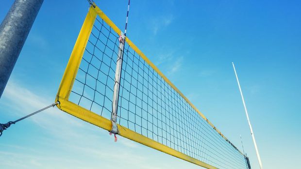 Beach volley net with yellow frame fixed on metal pole on seashore against blue sky