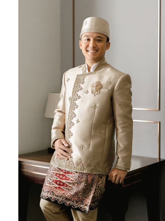 Auditya, sang mempelai pria, mengenakan beskap krem gading yang memancarkan kemewahan klasik. Potongan tegasnya diperkaya bordir emas di tepian, dengan motif tabur floral geometris yang harmonis. Foto: Instagram/@fcbweddings