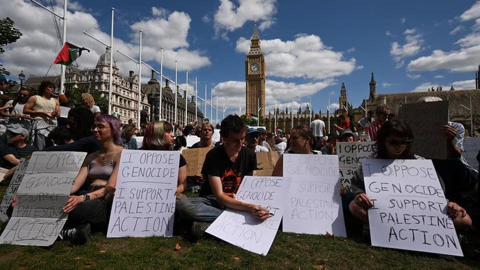 People holding signs sit during a rally organised by Defend Our Juries, challenging the British governments proscription of 