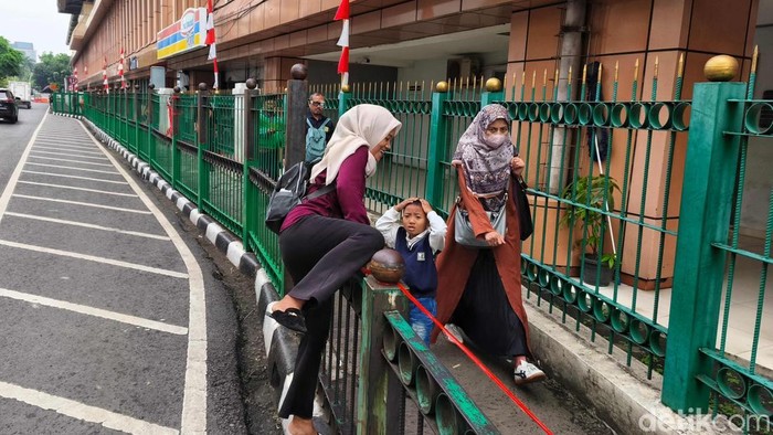 Sejumlah warga terlihat nekat melompati pagar Stasiun KAI Cikini, Jakarta Pusat, Selasa (12/8/2025). Aksi ini masih menjadi pemandangan sehari-hari.