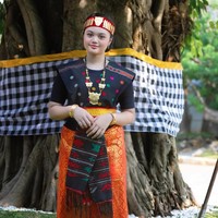 Amora Lemos tampil anggun mengenakan busana adat Batak lengkap, terdiri dari kain ulos berwarna hitam dengan motif merah, oranye, dan hijau, dipadukan dengan kain songket oranye keemasan yang dililit rapi di pinggang. Foto: Instagram/@amora_lemos05