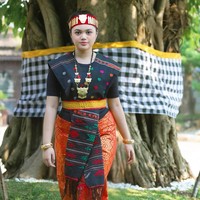 Penampilannya dipercantik dengan kalung emas besar berdesain khas, gelang emas di kedua tangan, serta manik-manik tradisional yang memperkuat nuansa adat. Foto: Instagram/@amora_lemos05