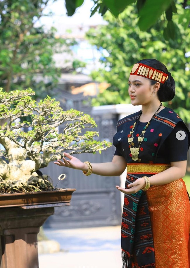 Rambut Amora disanggul rapi dengan sentuhan modern, dihiasi hiasan kepala merah dan emas yang menjadi ciri khas busana adat Batak, membuat penampilannya semakin megah. Foto: Instagram/@amora_lemos05