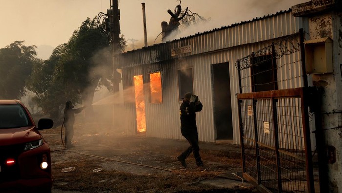 Firefighters work to extinguish a fire from a building during a wildfire, in Sichaina near Patras, Greece, August 13, 2025. REUTERS/Louiza Vradi