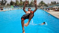 Seorang pemuda melompat dari tepi kolam, mencari sensasi segar di tengah suhu yang membakar. Foto: REUTERS/Khaled Abdullah