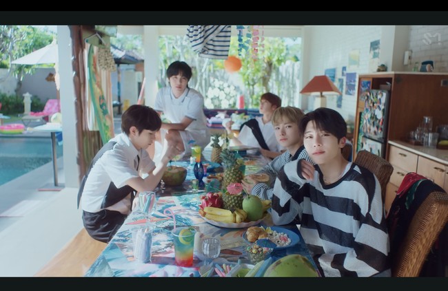 Tampak beberapa buah-buahan eksotis Indonesia sebagai properti seperti buah naga, pisang, kelapa, mangga, dan nanas dalam adegan personelnya berkumpul di meja makan, berbusana putih dan celana pendek. Foto: dok. SM Entertainment