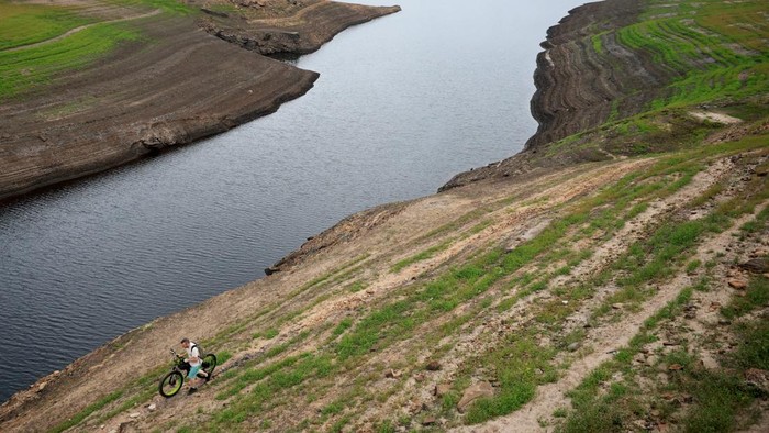 A man stands on an old Packhorse bridge which is usually submerged and has been exposed again after a prolonged period without rain led to water levels dropping at Baitings Reservoir near Ripponden, Britain, August 12, 2025. REUTERS/Phil Noble