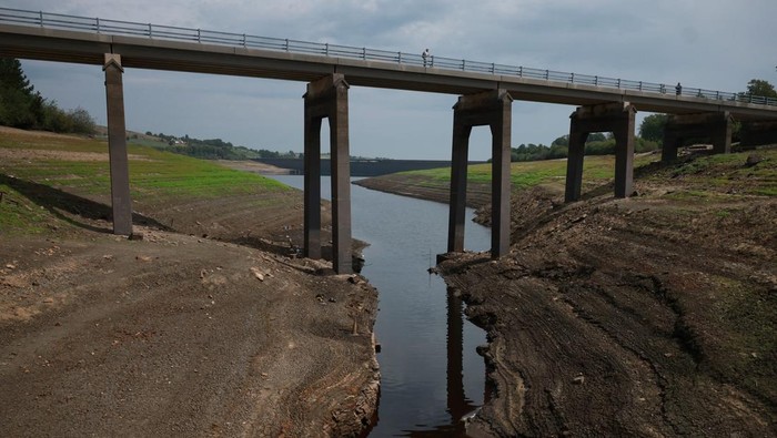 A man stands on an old Packhorse bridge which is usually submerged and has been exposed again after a prolonged period without rain led to water levels dropping at Baitings Reservoir near Ripponden, Britain, August 12, 2025. REUTERS/Phil Noble
