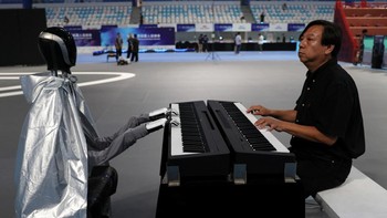 Seorang pria memainkan alat musik bersama robot humanoid jelang pembukaan World Humanoid Robot Games perdana di National Speed Skating Oval, Beijing, China, Kamis (14/8/2025). Kolaborasi ini menjadi simbol kemajuan teknologi robotika dalam bidang seni. REUTERS/Tingshu Wang  