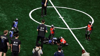 Wasit berdiri di tengah robot humanoid Booster Robotics T1 yang berlaga pada pertandingan sepak bola lima lawan lima di World Humanoid Robot Games perdana di National Speed Skating Oval, Beijing, China, Jumat (15/8/2025). Teknologi dan sportivitas berpadu dalam ajang ini. REUTERS/Tingshu Wang  