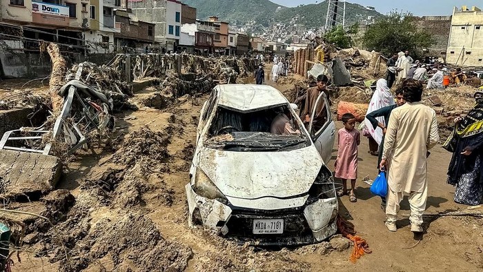 People gather near a damaged vehicle and scattered debris after the road washed out following a flash flood in Mingora, the main city of Swat Valley, in monsoon-hit northern Pakistans mountainous Khyber Pakhtunkhwa province on August 16, 2025. The death toll from heavy monsoon rains that have triggered flash floods across northern Pakistan has risen to at least 321 people in the last 48 hours, disaster agencies said on August 16. (Photo by Mehboob UL HAQ / AFP)