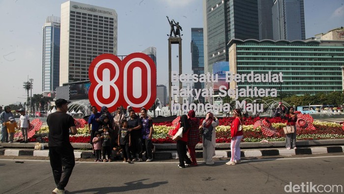 Warga berfoto dengan latar belakang instalasi HUT ke-80 RI di Bundaran HI, Jakarta, Minggu (17/8/2025).