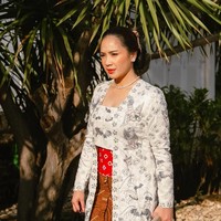 Nagita tampil anggun mengenakan kebaya brokat putih dengan detail bordir halus. Kebaya ini dipadukan dengan stagen merah bermotif, memberikan sentuhan kontras yang cantik. Foto: Instagram/@raffinagita1717