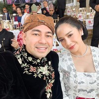 Nagita menyempurnakan penampilannya dengan kalung mutiara sederhana, anting kecil yang menawan, serta handbag putih yang memberi nuansa modern. Rambutnya disanggul rapi dengan hiasan bunga emas kecil di bagian belakang. Foto: Instagram/@raffinagita1717