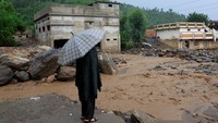 Seorang warga terlihat bertahan dengan payung di tengah derasnya aliran air yang melintasi area rusak. REUTERS/Akhtar Soomro