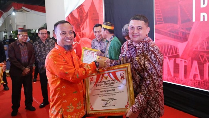 Gubernur Sulsel Andi Sudirman Sulaiman menyerahkan pengharagaan kepada Wali Kota Makassar Munafri Appi Arifuddin.