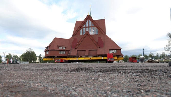 People look on, in front of Kiruna's old wooden church, which sits on a structure relocation rig with wheels for a two-day relocation trip to a new site next to a cemetery, to save its wooden walls from ground subsidence and the expansion of the world's largest underground iron ore mine, in Kiruna, Sweden August 19, 2025. REUTERS/Leonhard Foeger