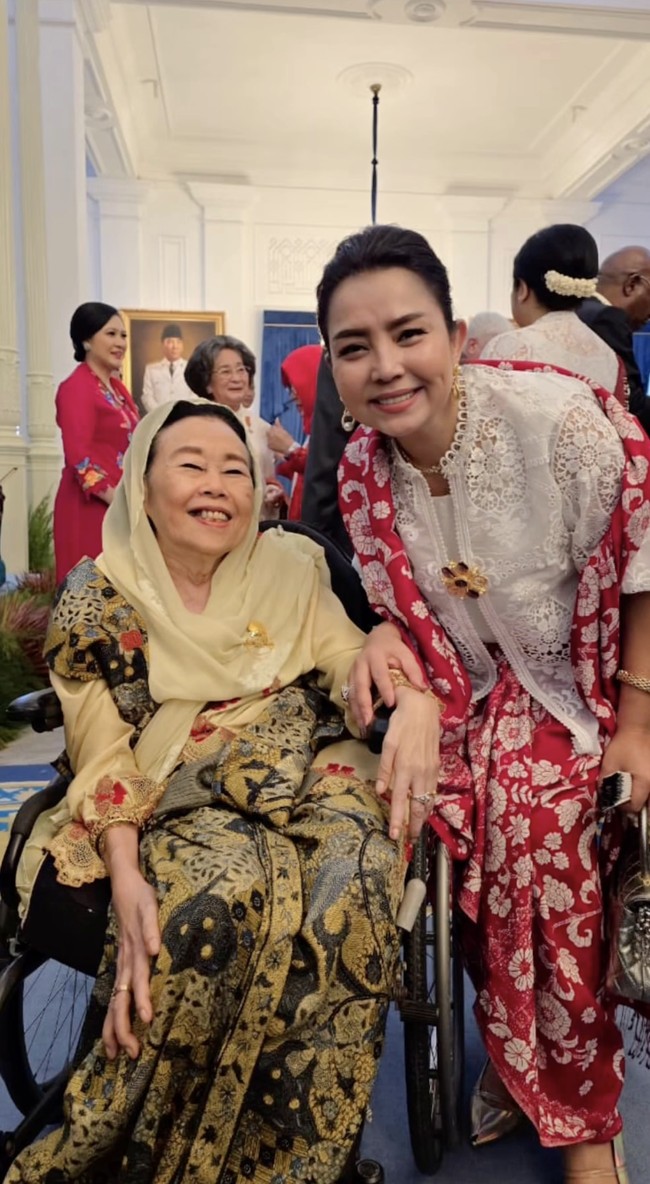 Mayangsari tampil anggun kenakan atasan putih berbahan brokat dengan detail bordir bunga yang indah. Atasan tersebut dipadukan dengan bawahan kain merah bermotif, memberi kesan mewah dan tradisional. Foto: Instagram/@mayangsari_official